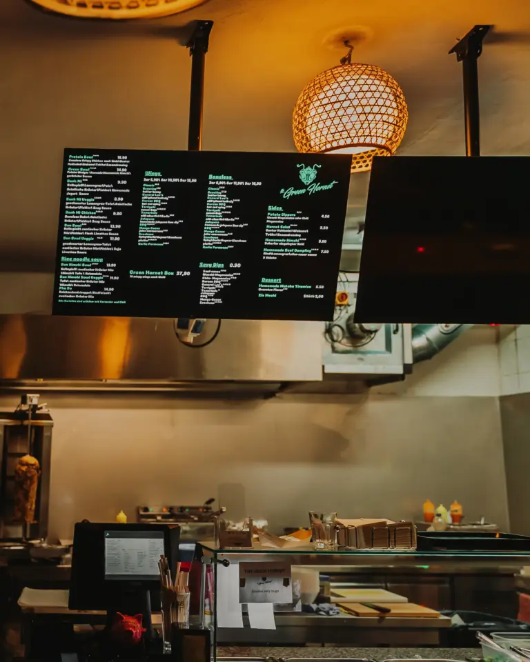 Leuchtende digitale Speisekarte mit verschiedenen Gerichten und Preisen in einer Restaurantküche unter einer runden Deckenlampe