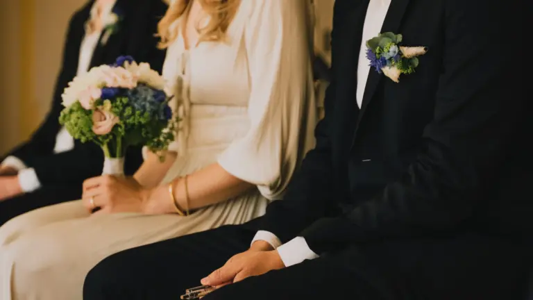 Brautpaar und Trauzeuge sitzen nebeneinander, Braut hält einen Blumenstrauß, Bräutigam trägt Anzug mit Ansteckblume