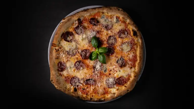 Pizza mit knusprigem Rand, belegt mit Käse, Salami und Basilikumblättern in der Mitte