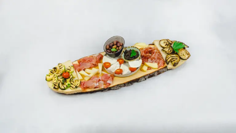 Antipasti-Platte mit gegrilltem Gemüse, Schinken, Käse, Oliven und Tomaten auf rustikalem Holzbrett