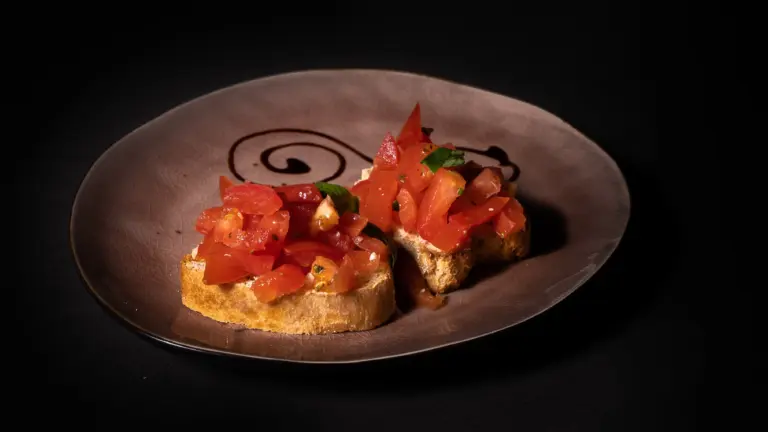 Zwei Bruschetta mit gewürfelten Tomaten und Kräutern auf einem braunen Teller mit schwarzer Spirale