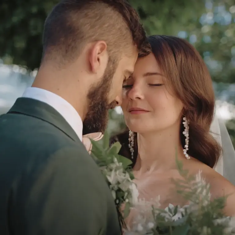 Brautpaar in Hochzeitskleidung steht nah beieinander, die Braut trägt lange Ohrringe und hält einen Blumenstrauß
